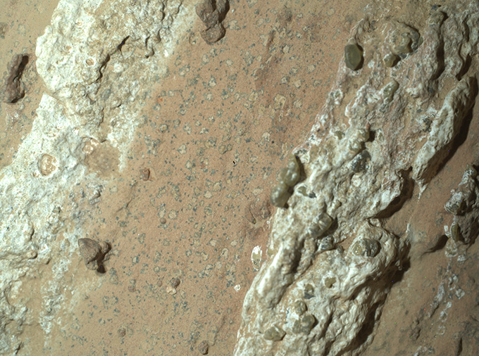 A close-up view of reddish dirt, with yellow crystals emerging from broken rocks in the middle